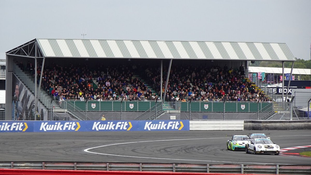 Gradería techada llena de público frente a la recta de un circuito durante una carrera