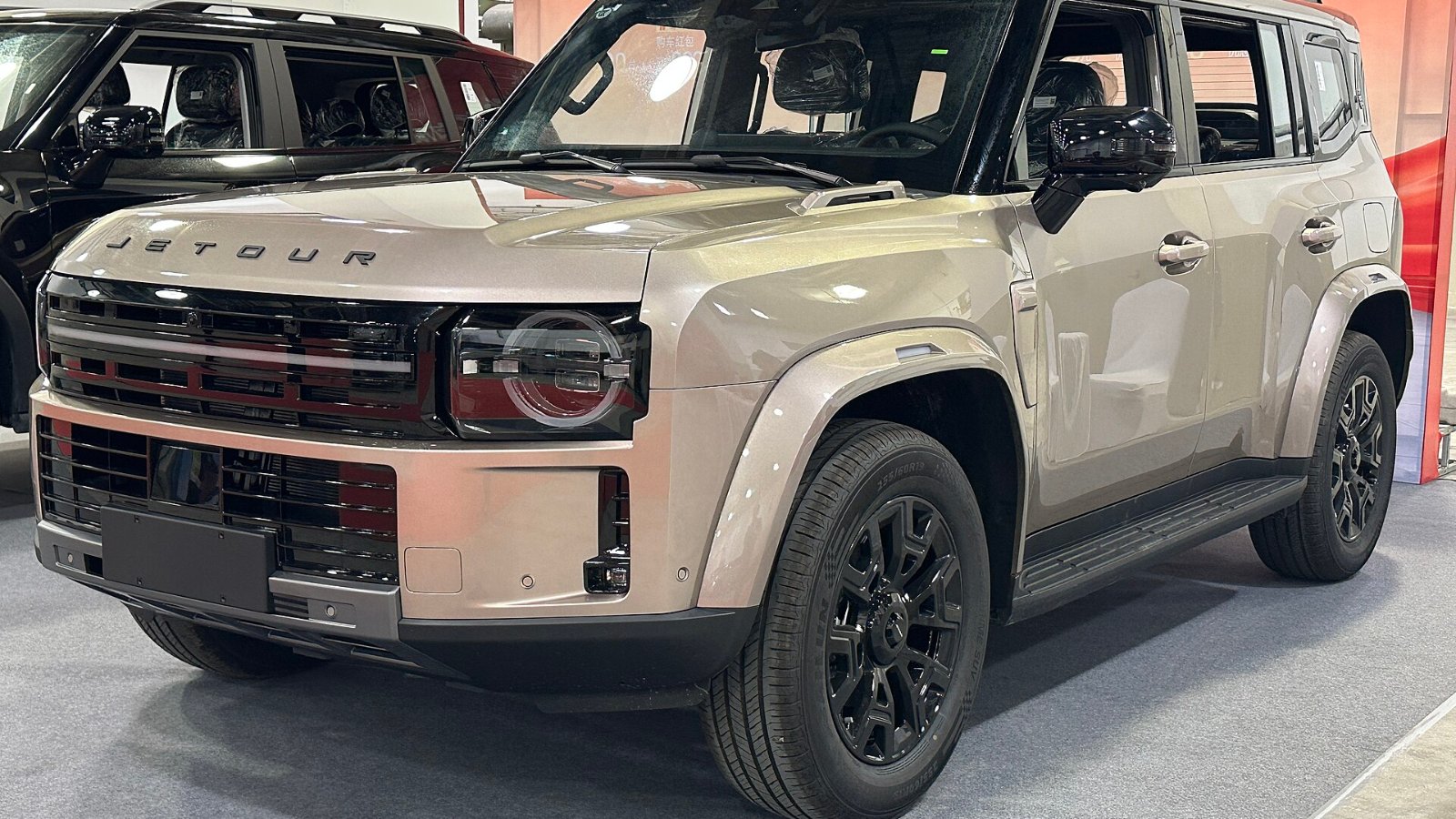JETOUR Traveler 7 color beige con rines negros, visto de tres cuartos delantero en una exhibición