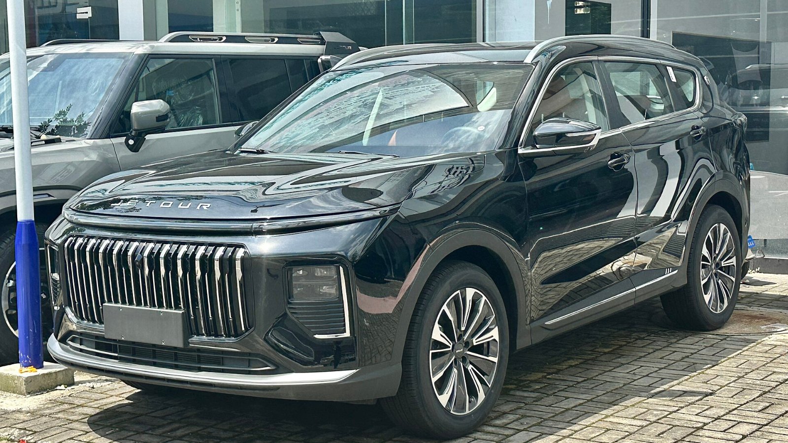 JETOUR X70 PLUS negro con parrilla de barras verticales, estacionado frente a un concesionario en China