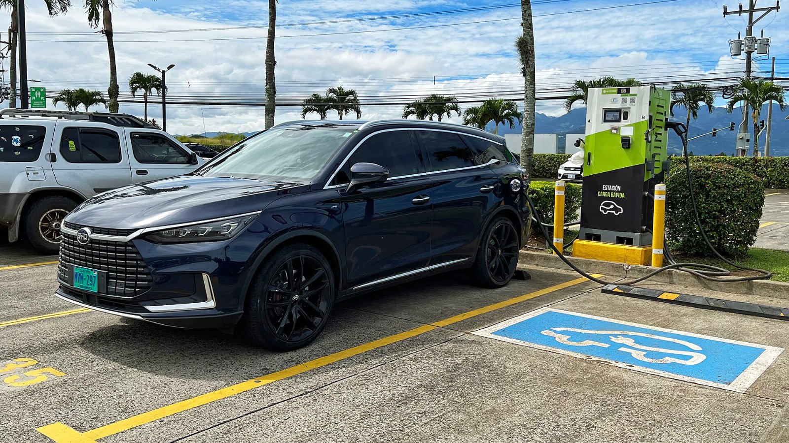BYD Tang EV azul oscuro conectado a un cargador rápido verde en un estacionamiento con palmeras en Alajuela, Costa Rica